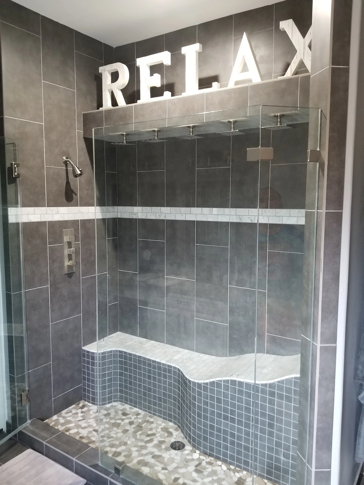 Luxurious bathroom remodel featuring custom shower with RELAX signage, curved bench seating, and modern tile work